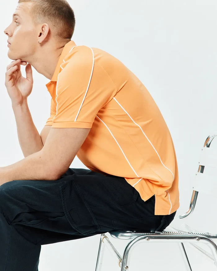 Mens Rhys Sport Polo in vibrant peach pique knit, featuring a classic fit, two-button placket, and distinctive white piping along the shoulders and sides, with side vents.