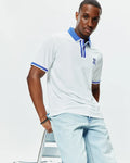 Mens Ridley Pique Polo, white classic fit pique polo with royal blue ribbed collar, striped placket, and cuffs, featuring a medium embroidered royal blue Psycho Bunny skull logo on the left chest.