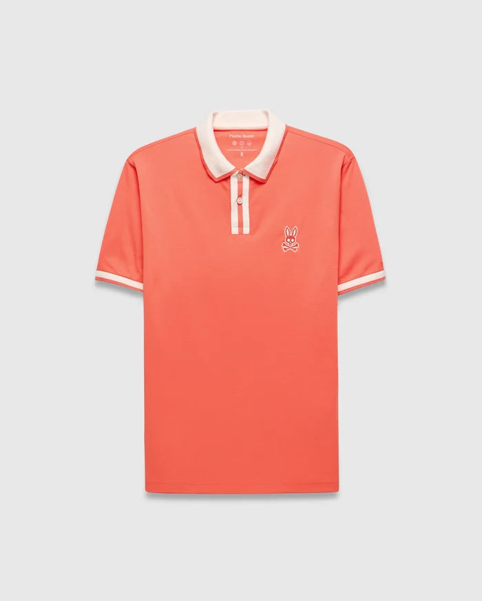 Mens Ridley Pique Polo in coral pique, featuring a classic fit, cream ribbed collar and cuffs with stripes, a two-button placket with cream stripe, and an embroidered white Psycho Bunny skull logo on the left chest.