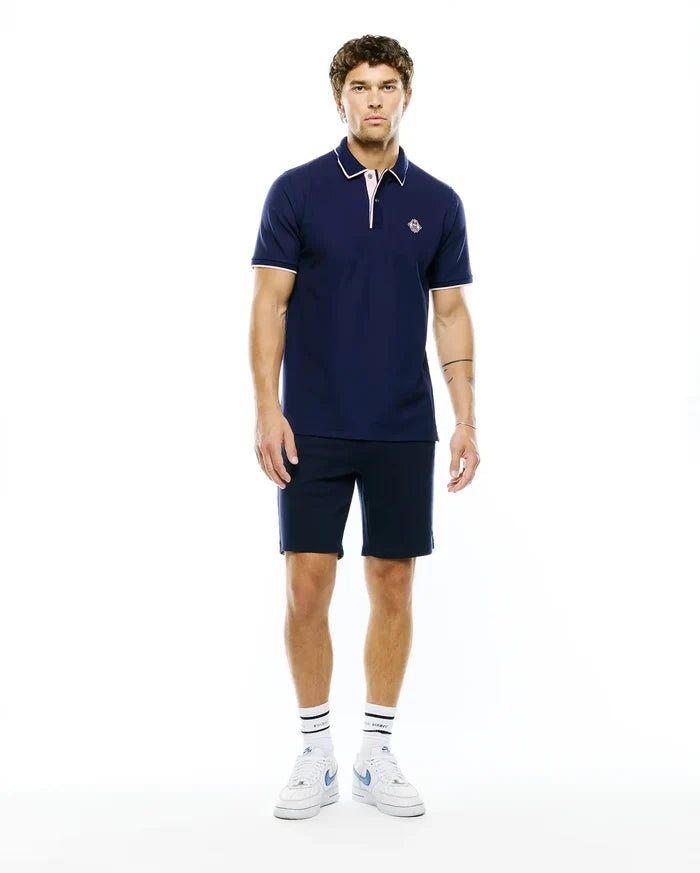 MENS ROBIN PIQUE POLO in navy, classic fit, with white collar tipping, pink placket and cuff trim, and a small embroidered Psycho Bunny skull logo on the left chest.
