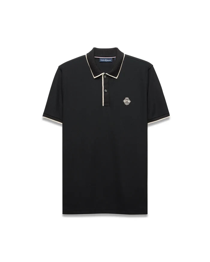 Mens Robin Pique Polo, black classic fit with cream piping on the collar and cuffs, featuring a textured pique fabric and an embroidered Psycho Bunny skull logo on the left chest.