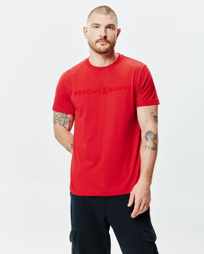 Mens Royce Graphic Tee, a vibrant red classic fit jersey knit t-shirt with a large, tonal Psycho Bunny text and iconic bunny skull graphic prominently displayed on the chest.