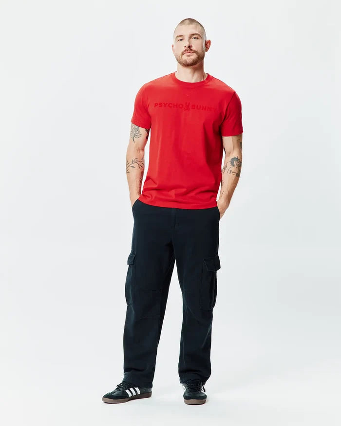 Mens Royce Graphic Tee, a classic fit red jersey t-shirt featuring a large, tonal embossed Psycho Bunny text logo with the bunny skull centered on the chest.