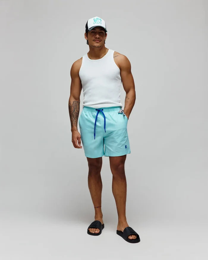 Mens Samos Hydrochromic Printed Swim Trunk in aqua with royal blue drawstring and small embroidered Psycho Bunny logo. Complemented by a white ribbed tank, a white and black cap with a large teal bunny skull, and black Psycho Bunny slides.