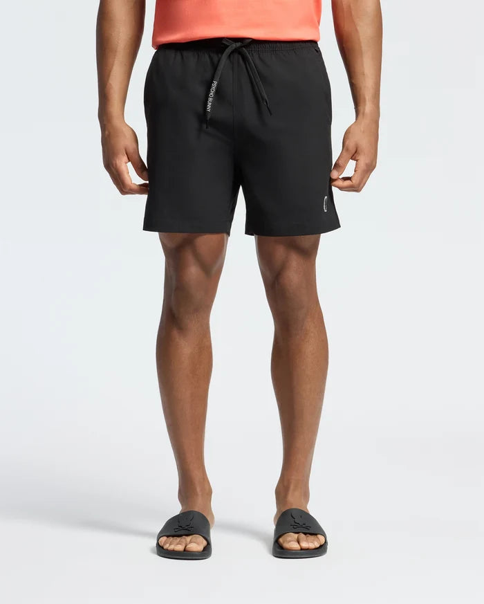 Black Mens Samos Hydrochromic Printed Swim Trunk with a classic fit, featuring a smooth fabric, white PSYCHO BUNNY text on the drawstring, and a small silver bunny skull logo on the lower left leg.