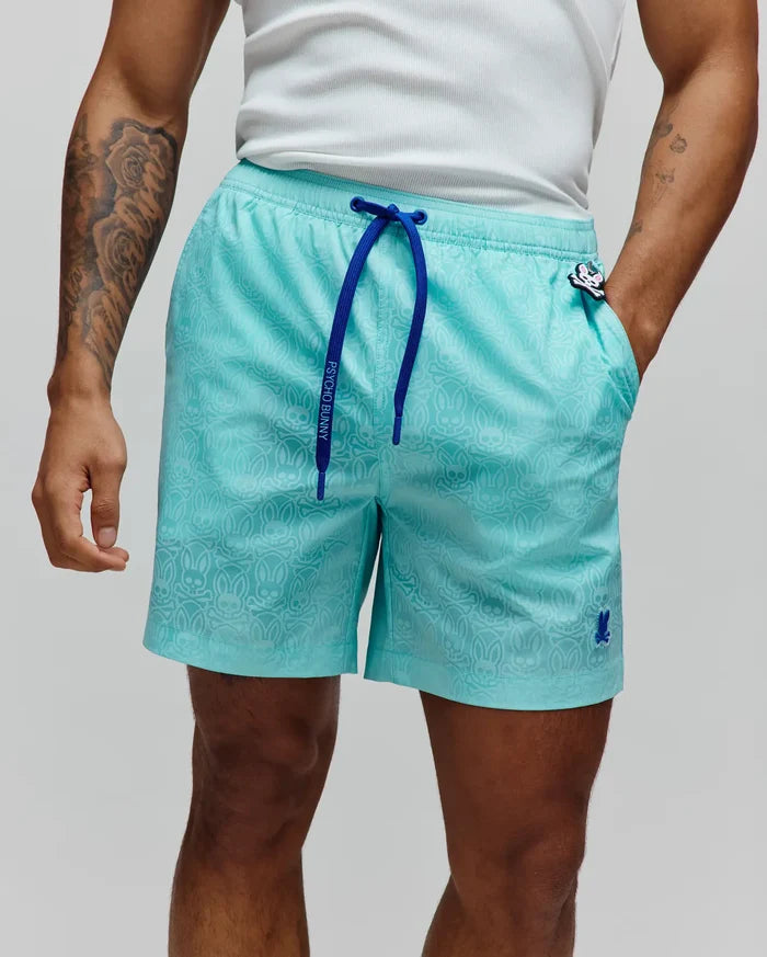 Mens Samos Hydrochromic Printed Swim Trunk in aqua, relaxed fit, subtle all-over bunny skull print. Royal blue drawstring with Psycho Bunny text, embroidered bunny skull on left leg, and bunny skull charm on right pocket.