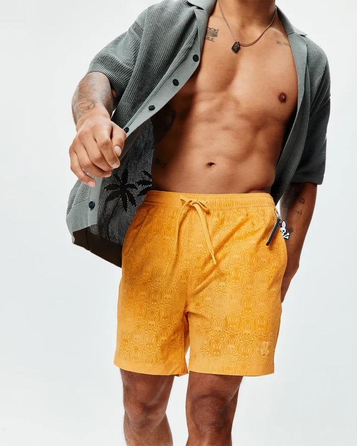 Mens Samos Hydrochromic Printed Swim Trunk in vibrant orange, featuring an all-over subtle hydrochromic Psycho Bunny skull and crossbones print, drawstring waist, and small embroidered bunny logo on the left leg, offering a relaxed fit.