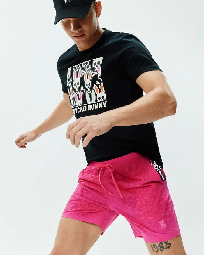 Black jersey t-shirt with a large Psycho Bunny skull graphic, paired with bright pink Mens Samos Hydrochromic Printed Swim Trunk 6, featuring a tonal bunny skull pattern, drawstring, and embroidered logo.