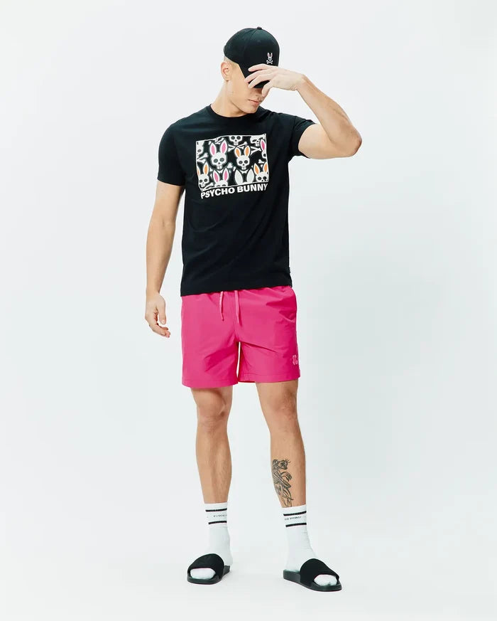 Black jersey t-shirt with a colorful Psycho Bunny skull graphic, bright pink Mens Samos Hydrochromic Printed Swim Trunk 6 with a tonal bunny logo, and a black cap with a pink embroidered bunny.