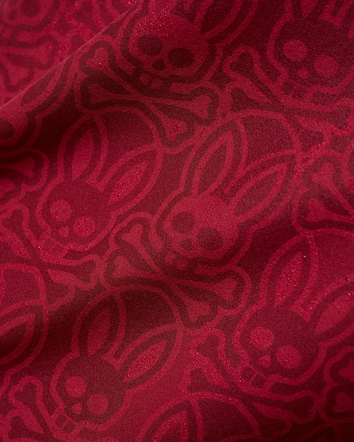 Mens Samos Hydrochromic Printed Swim Trunk in rich red, featuring an all-over darker red hydrochromic Psycho Bunny skull and crossbones pattern on smooth fabric.
