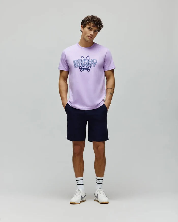 Lavender jersey t-shirt with a large, distressed blue and purple Psycho Bunny skull logo on the chest, paired with classic fit navy Mens Shiro Twill Short.