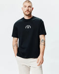Mens Stevie Relaxed Fit Tee in black, featuring a small white Psycho Bunny skull and crossbones logo with arched text centered on the chest, made from smooth jersey knit fabric.