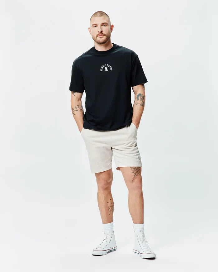 Black Mens Stevie Relaxed Fit Tee, soft jersey, with a small white Psycho Bunny skull logo and text on the chest, paired with light beige shorts featuring a small embroidered white bunny logo on the left thigh.