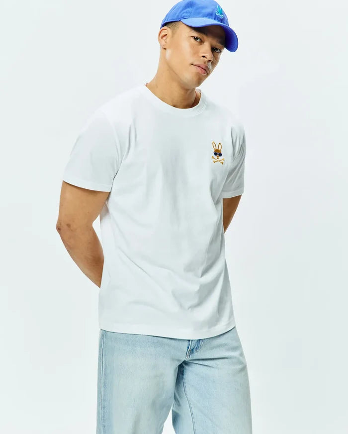Mens Sunny Chest Graphic Tee, a classic fit white jersey t-shirt featuring a small embroidered brown Psycho Bunny skull logo with blue sunglasses and crossbones on the left chest.