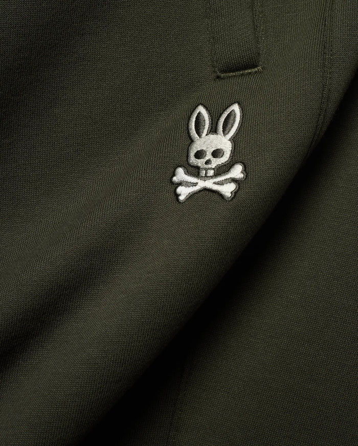Mens Terrence Brushed Fleece Sweatpant in dark olive green, featuring a small, intricately embroidered white and silver Psycho Bunny skull logo on the upper leg, showcasing the soft brushed fleece knit texture.