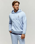 Mens Timothy 4k Bunny Hoodie, a light blue classic fit jersey hoodie with a kangaroo pocket, black drawstrings, and a small embroidered Psycho Bunny skull logo on the left chest.