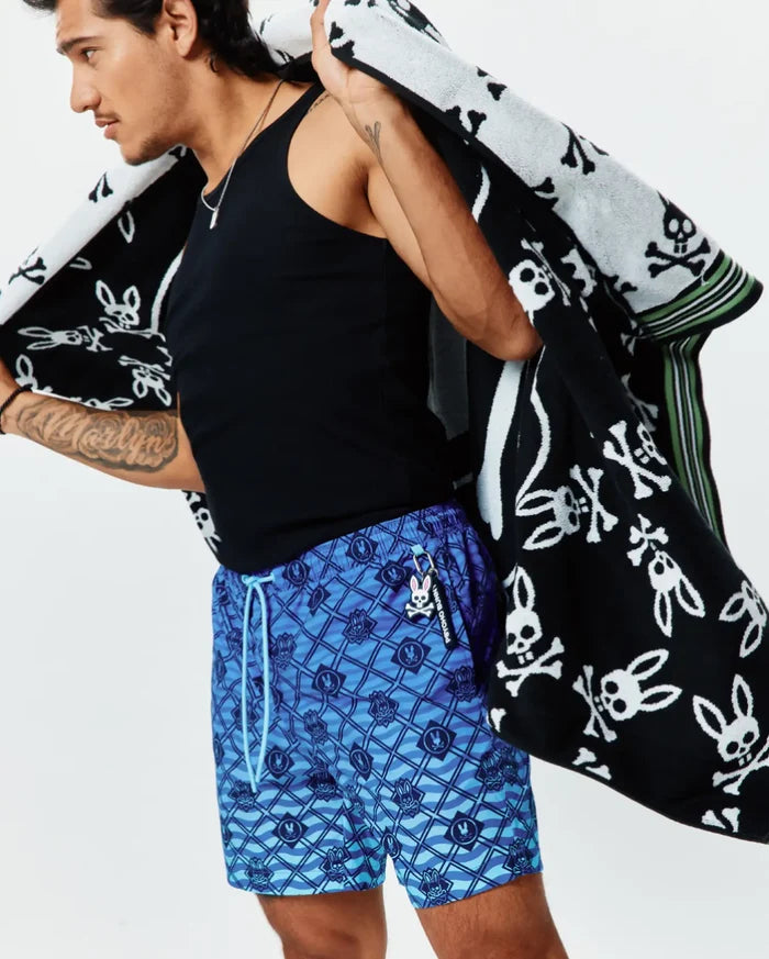 Mens Tobias Gradient Swim Trunk featuring an all-over blue geometric wave pattern with integrated small Psycho Bunny skull logos, light blue drawstring, and a Psycho Bunny keychain.