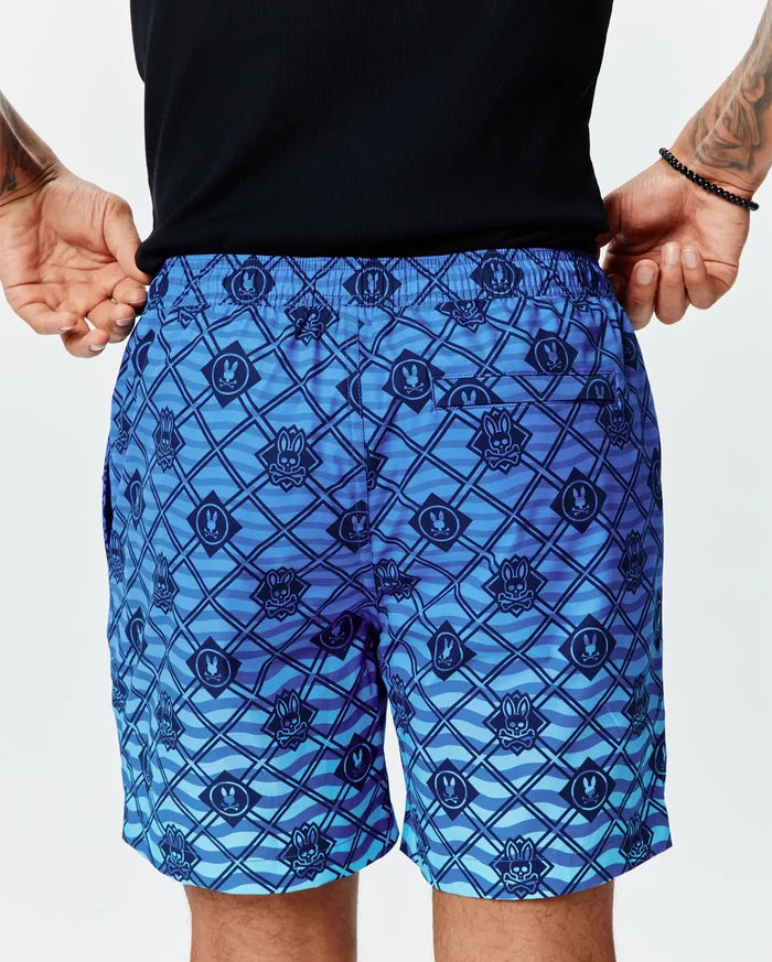 Mens Tobias Gradient Swim Trunk in a blue gradient with an all-over dark blue Psycho Bunny skull logo and diagonal grid pattern over a wavy background on smooth, relaxed-fit quick-dry fabric.