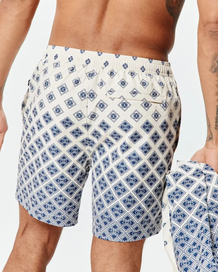 Mens Tobias Swim Trunk in cream with a navy blue all-over geometric pattern featuring the small Psycho Bunny skull logo, classic fit, smooth quick-dry fabric, and a back pocket.
