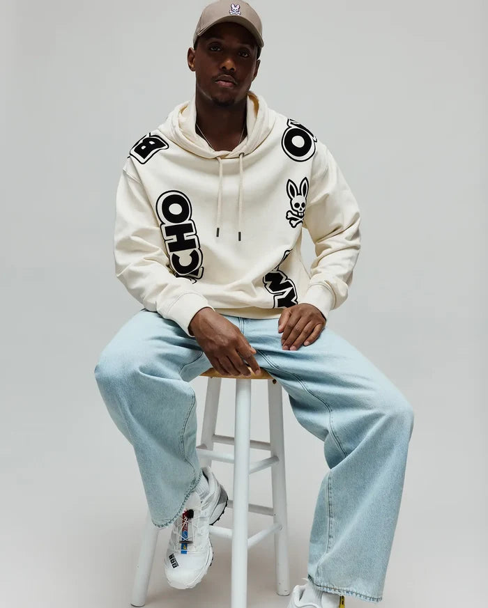 Mens Toby Oversized Hoodie in cream, featuring bold black scattered PSYCHO BUNNY lettering and a prominent bunny skull logo on the left chest, made from soft fleece.
