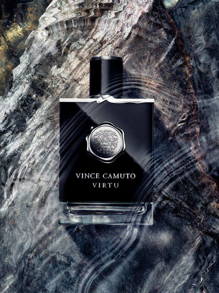 A bottle of Vince Camuto Men’s Virtu 3.4 oz Eau de Toilette Spray rests on a textured, marbled surface while water ripples flow across the scene, creating a dynamic and luxurious effect that perfectly captures the bold, sophisticated essence of this men’s fragrance.