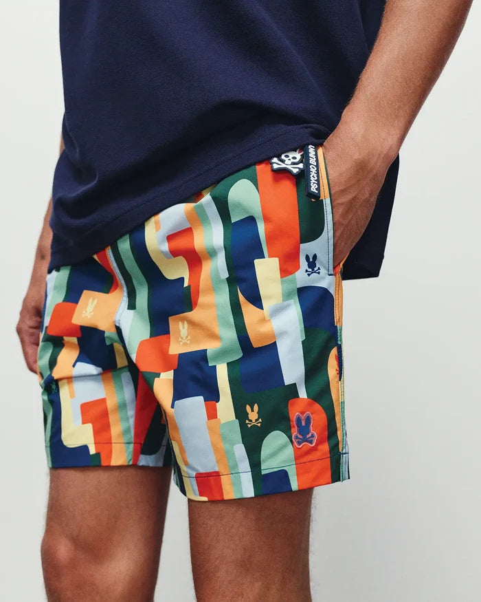 Mens Wes All Over Print Swim Trunk by Psycho Bunny, showcasing a vibrant multi-color abstract geometric pattern with integrated skull logos and a prominent branded side tag, classic fit.