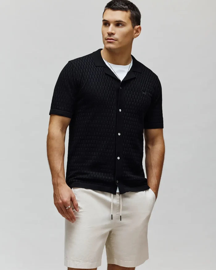 Mens Xandros Knit Shirt, black textured checkerboard knit with a classic fit, spread collar, full white button placket, and a small embroidered Psycho Bunny skull logo on the left chest.