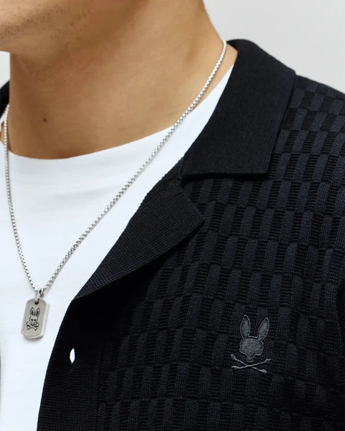Mens Xandros Knit Shirt, black, featuring a refined checkerboard knit texture, classic collar, and a small tonal embroidered Psycho Bunny skull logo on the left chest.