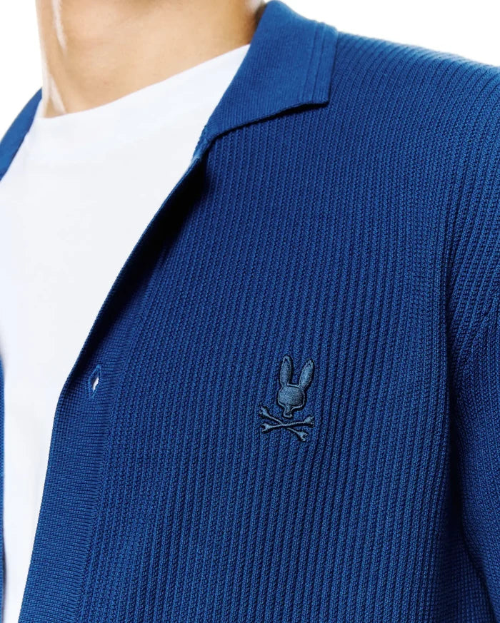 Mens Yann Knit Shirt: Deep blue ribbed knit shirt with a relaxed fit, featuring an open collar and a small, embroidered dark blue Psycho Bunny skull logo on the left chest.