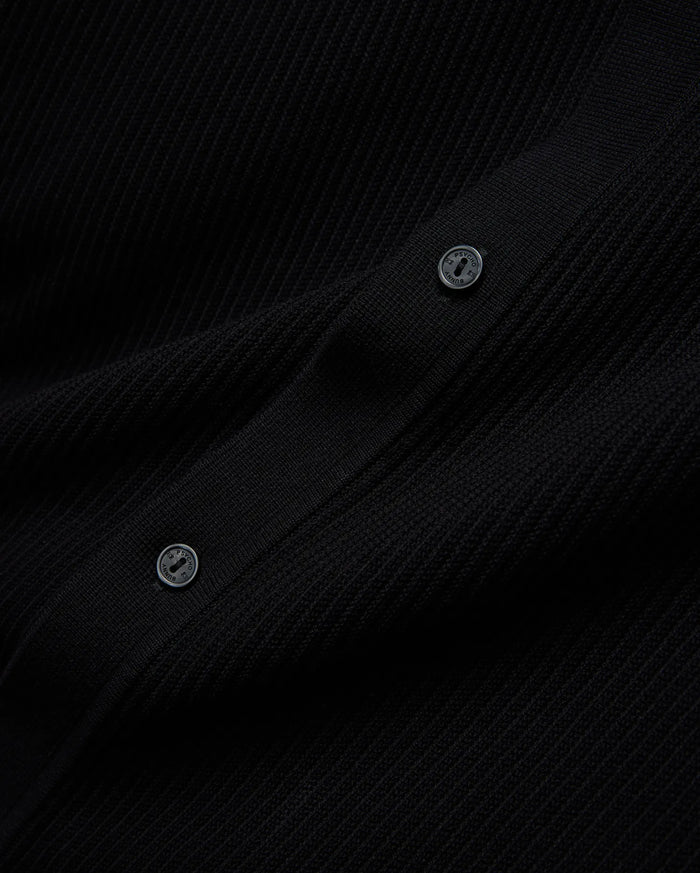 Mens Yann Knit Shirt, a sleek black premium ribbed knit garment, detailed with two dark buttons featuring the Psycho Bunny brand name embossed in a lighter tone.