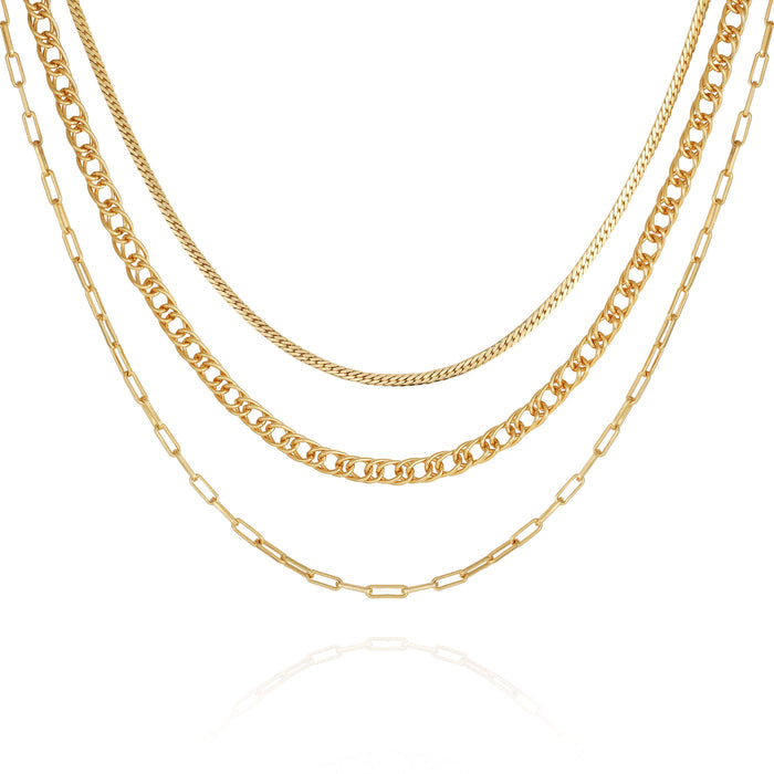 Four gold chains from the Vince Camuto Multi Layered Chain Necklace, featuring varied link styles—including a sleek snake chain and an elegant wheat chain—hang side by side on a white background to create a stylish layered look. Each chain showcases unique thicknesses and designs, lending a sophisticated, modern appeal.