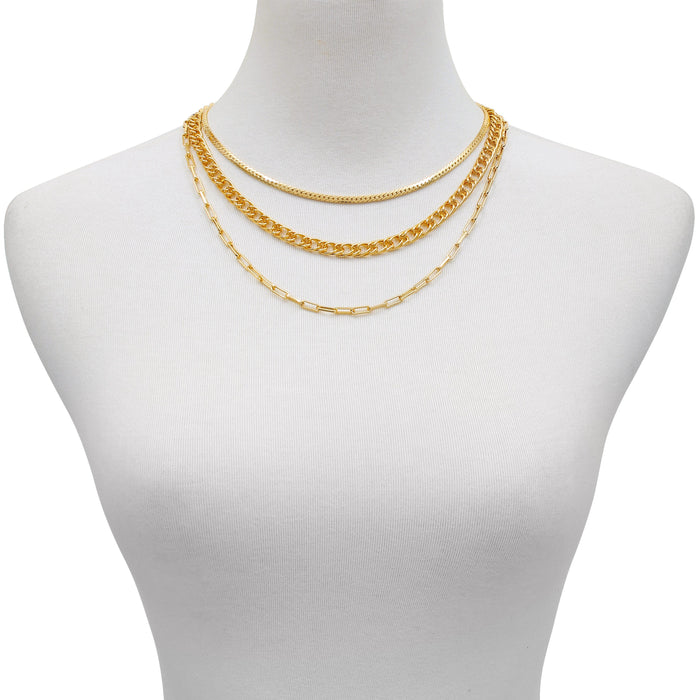 A white mannequin showcases the Vince Camuto Multi Layered Chain Necklace, featuring three gold necklaces—a paper clip chain, a wheat chain, and a snake chain—in varying styles and lengths, set against a plain background.