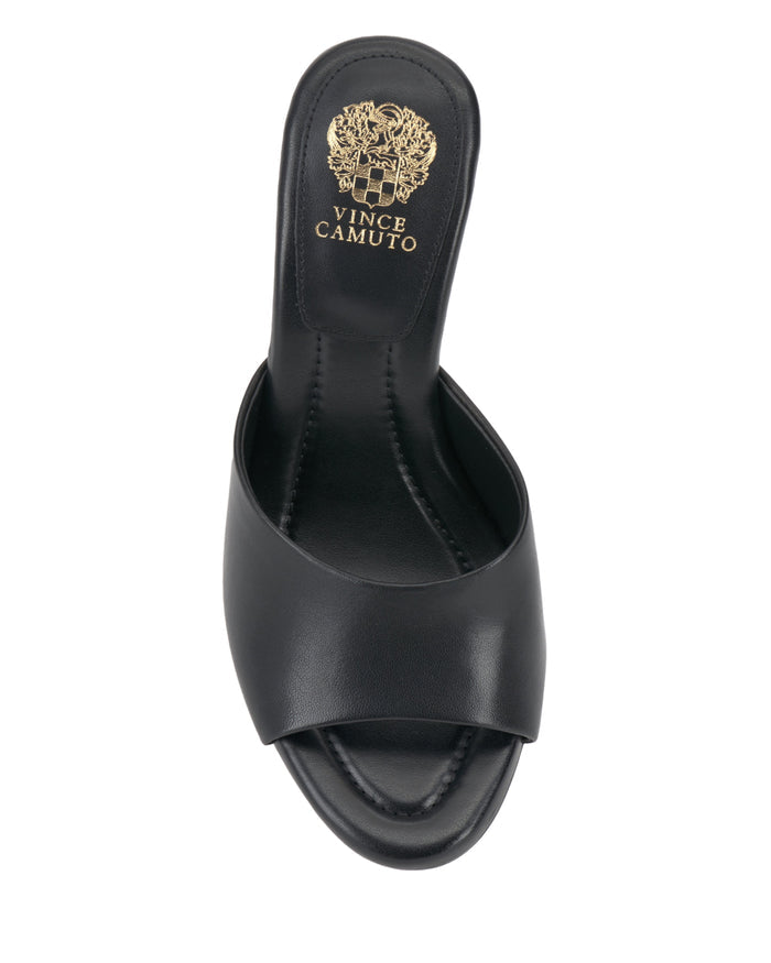 The Vince Camuto Paigely Mule is a black leather slide sandal with a wide toe strap, open toe, and gold logo emblem on the insole, shown from a top-down view. This minimalist design features a chic flared heel and comfortable pillow footbed for effortless style all day long.