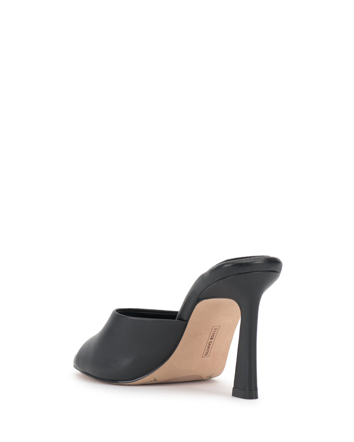 The image shows the Paigely Mule by Vince Camuto—a black minimalist mule shoe with a flared heel and beige sole—displayed from the back on a white background.