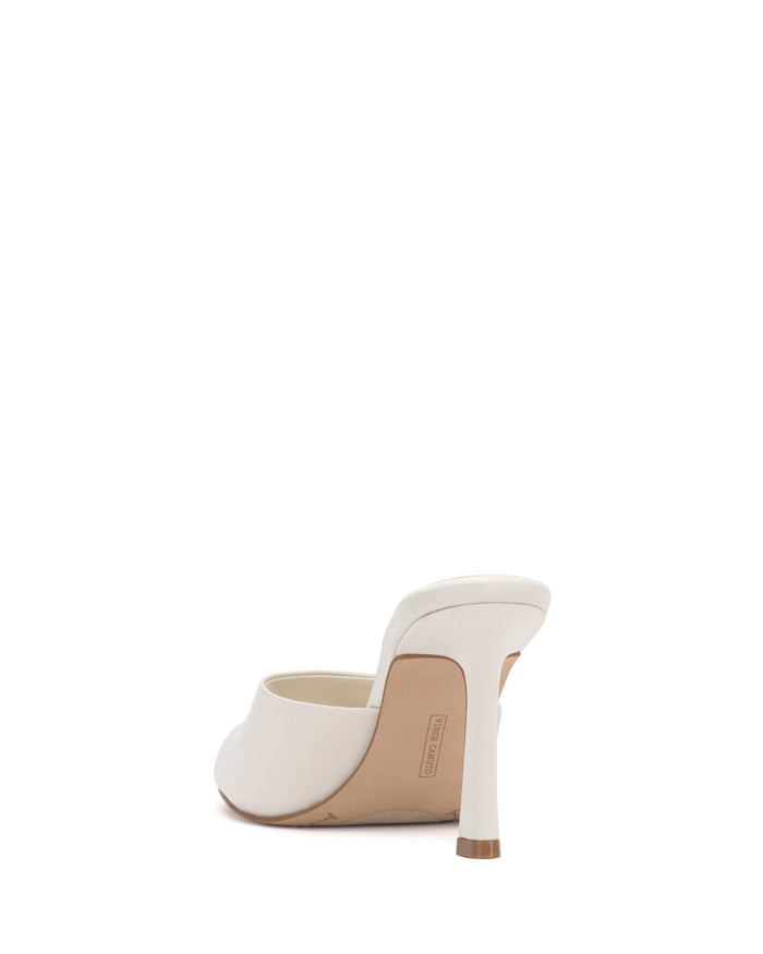 The Vince Camuto Paigely Mule is a white leather stiletto-heeled sandal, pictured from the back, showcasing a square toe, single wide strap, slim flared high heel, and tan outsole. Designed with a pillow footbed for cushioned comfort.