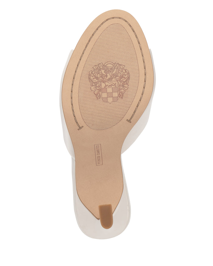The image displays the beige sole of the Vince Camuto Paigely Mule, a white satin shoe featuring a small brown heel tip. An intricate emblem and the MADE IN ITALY label appear on the bottom, emphasizing its elegance and quality craftsmanship.