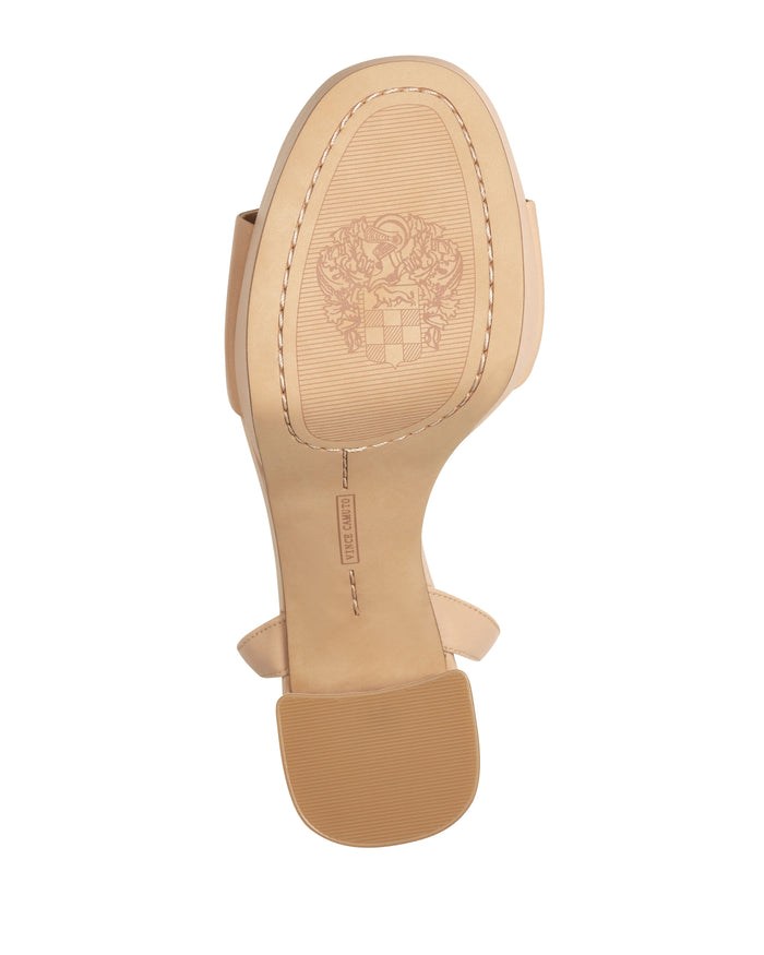 Bottom view of the nude Pendry Platform Sandal by Vince Camuto, reminiscent of classic 70s sandals, featuring a tan outsole with an embossed crest logo and brand name label on the heel.