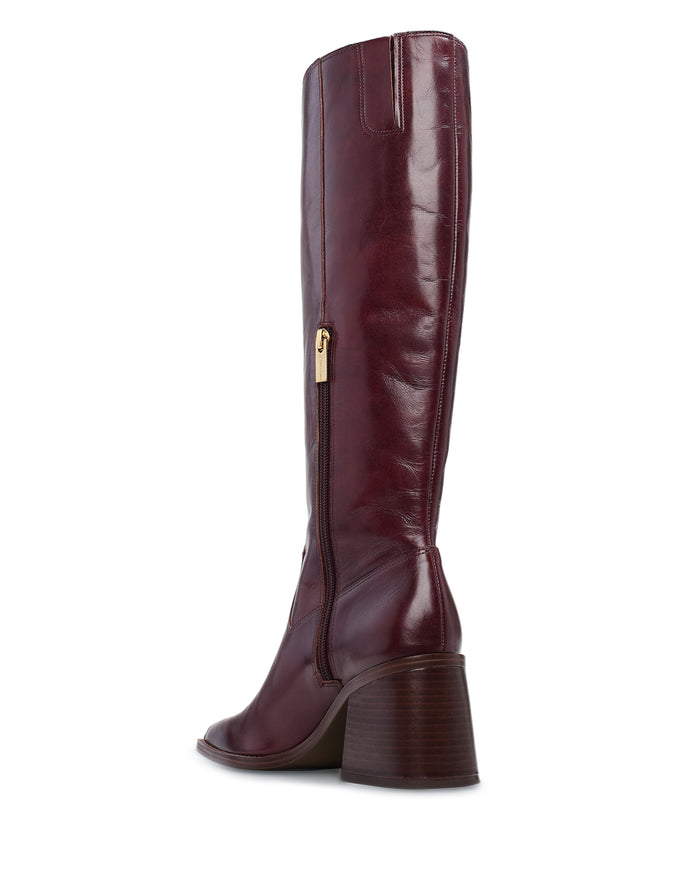 A tall, dark burgundy Vince Camuto Sangeti Wide Calf Boot crafted in leather with a gold side zipper and a chunky, stacked brown heel, displayed from a rear-side angle on a white background.