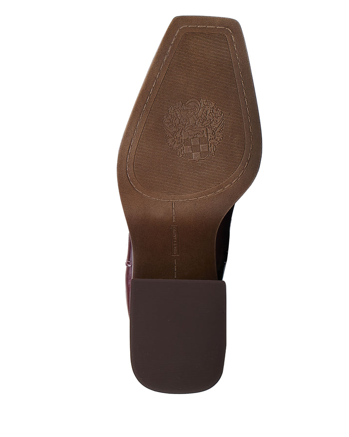The image shows the sole of a brown shoe with a square toe, featuring a detailed embossed crest or emblem near the heel area. This elegant design is characteristic of the Sangeti Wide Calf Boot by Vince Camuto, renowned for its sophistication and quality craftsmanship.