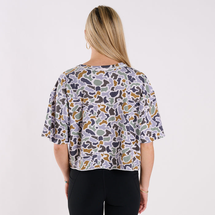 Woman wearing a boxy camo printed shirt on a grey background.