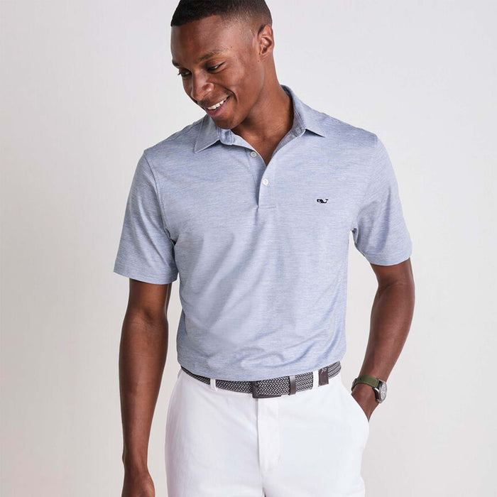 Vineyard Vines Men's Short Sleeve Polo in Hammerhead, sizes S-XXL. Front view of a man wearing the polo tucked into white pants with a woven belt, smiling. Color is a muted blue.
