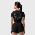 Black cropped tee with white wing graphic on back, worn by model, rear view
