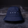 flatlay WN'22 Cinch Bucket Hat in navy blue, front view on dark surface