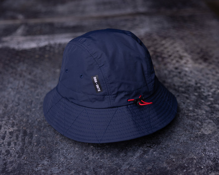 flatlay WN'22 Cinch Bucket Hat in navy blue, top view on textured surface