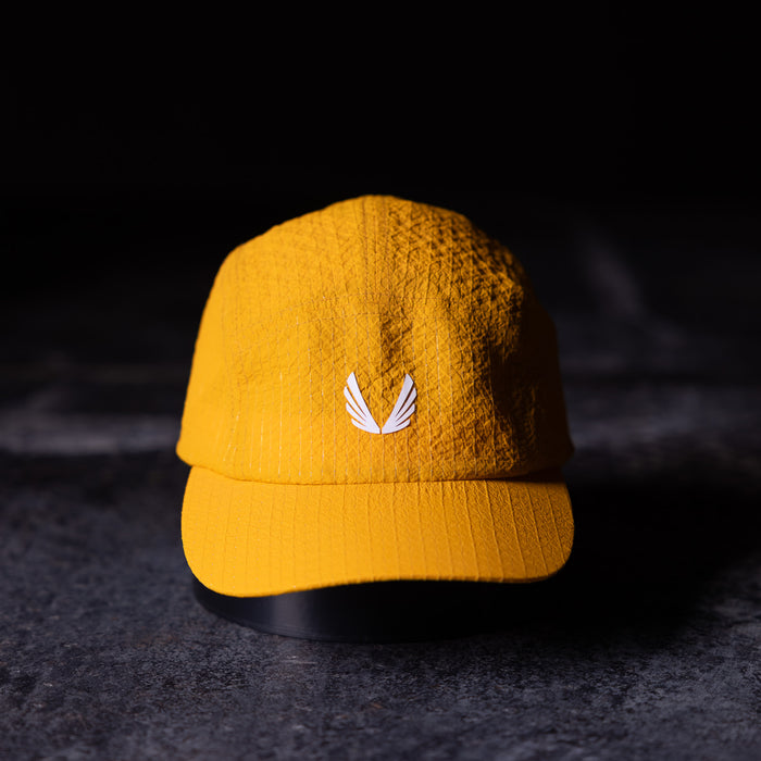 flatlay WN'23 5 Panel Hat in golden yellow, front view on dark surface