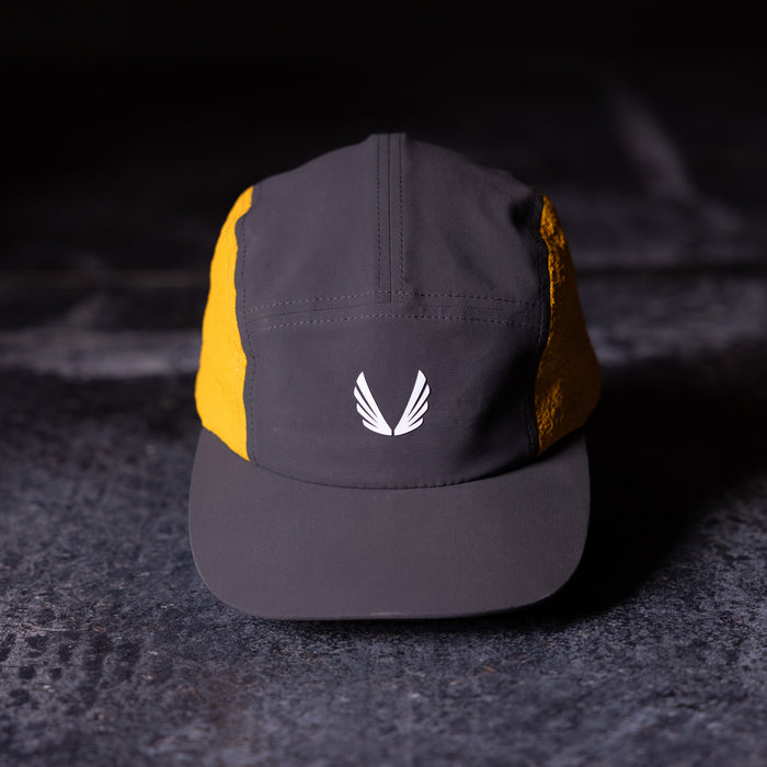 Flatlay of Two Tone 5 Panel Hat in charcoal and gold with white wing logo, front view