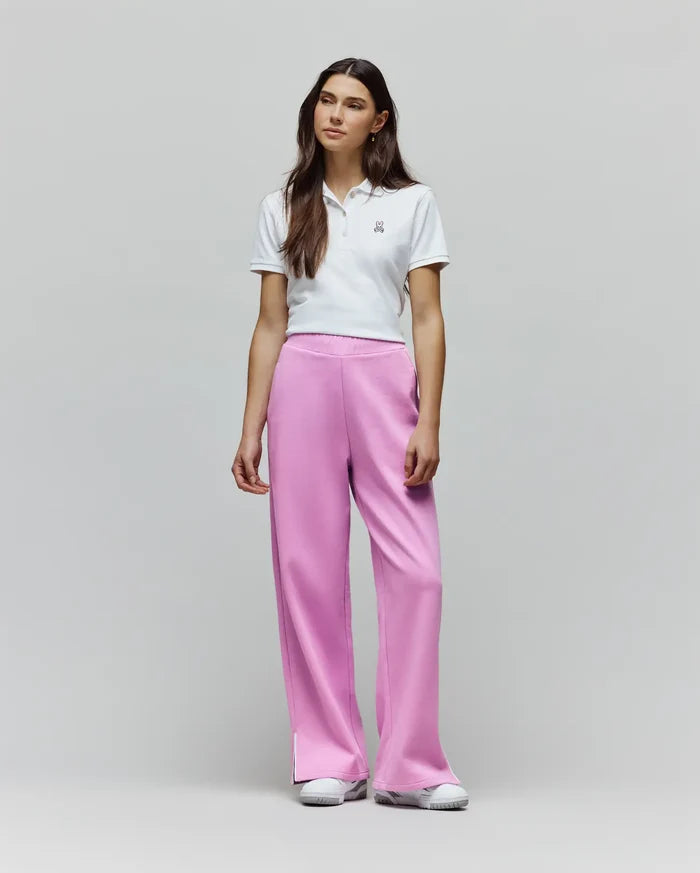 White cropped pique polo with embroidered Psycho Bunny logo, paired with Womens Daisie Fleece Joggers in vibrant pink, featuring a relaxed wide-leg fit and subtle side split detail.