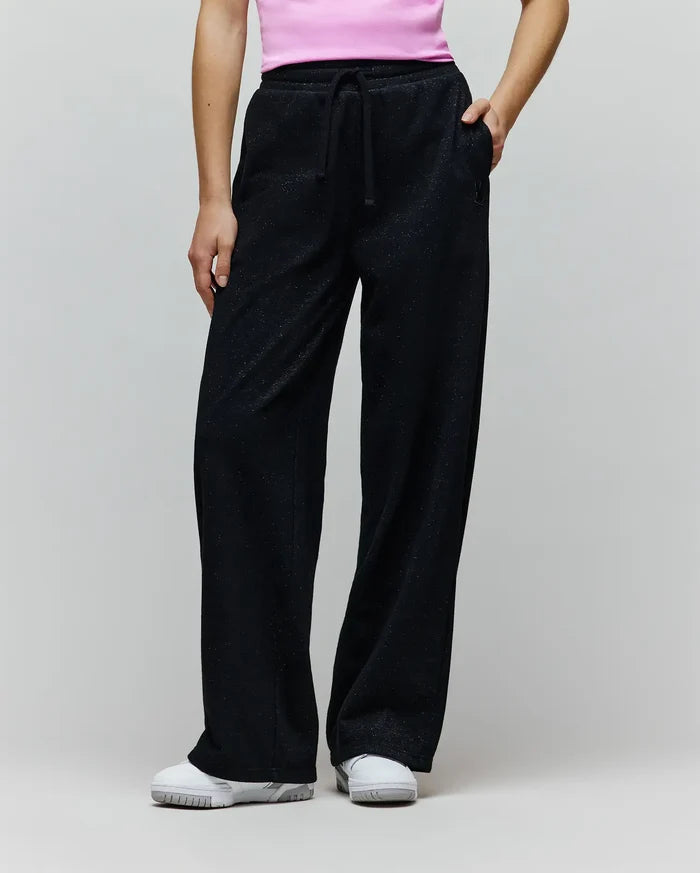 Womens Jules Lurex Sweatpant in black, featuring a relaxed wide-leg fit, shimmering lurex knit fabric, drawstring waist, and a small embroidered Psycho Bunny skull logo near the right pocket.
