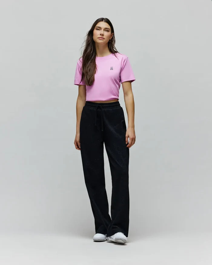 Pink cropped jersey t-shirt with a small embroidered Psycho Bunny skull logo on the left chest, paired with black Womens Jules Lurex Sweatpant featuring a relaxed wide-leg fit and subtle shimmer.