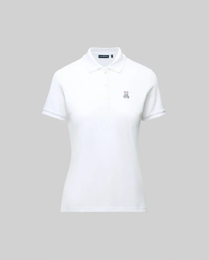 The WOMENS PIQUE POLO - WT0100003 by Psycho Bunny is a white short-sleeve polo featuring a collar, button placket, and 4k-stitch embroidered Bunny logo on the left chest, shown on a plain gray background.